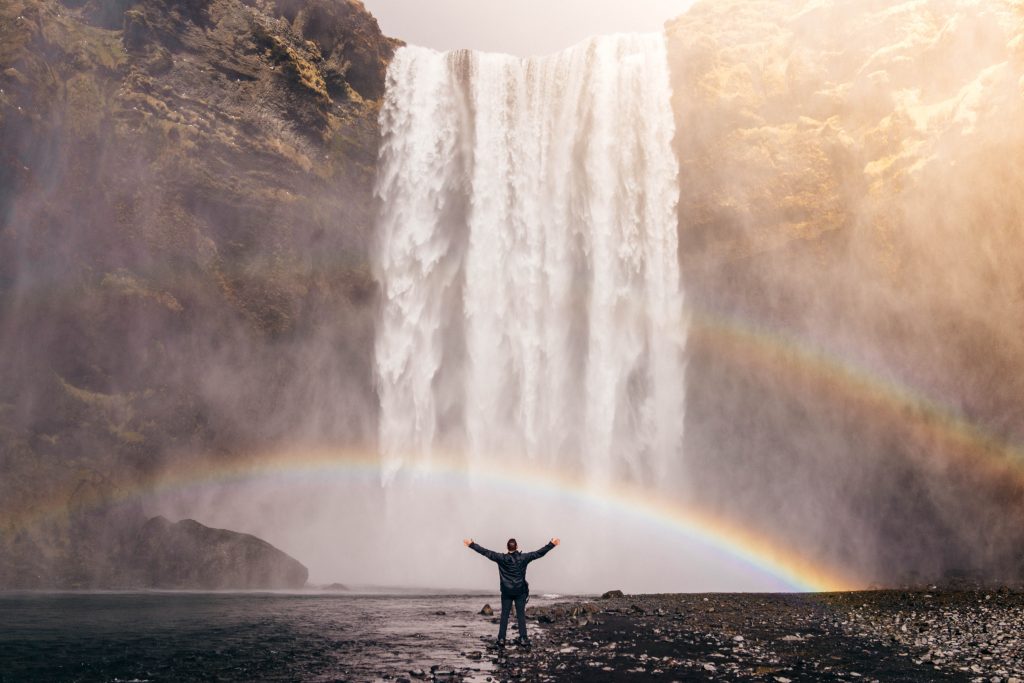 man arms open waterfall rainbow